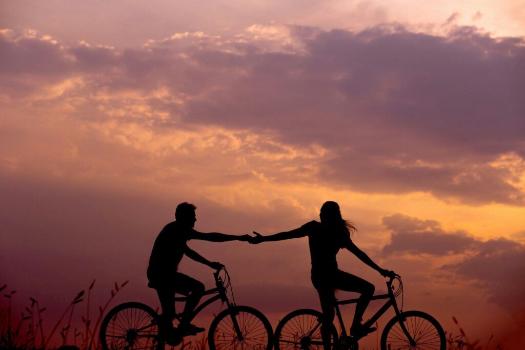 Couple riding bikes side by side, reaching for each other's hand at sunset